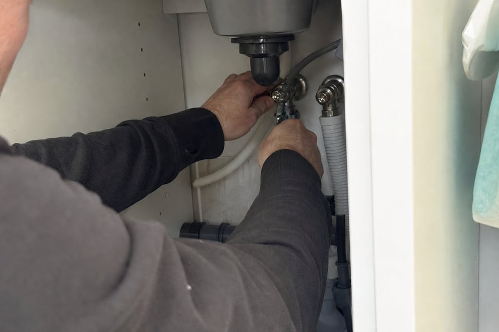 plombier qui resserre un raccord sous un évier